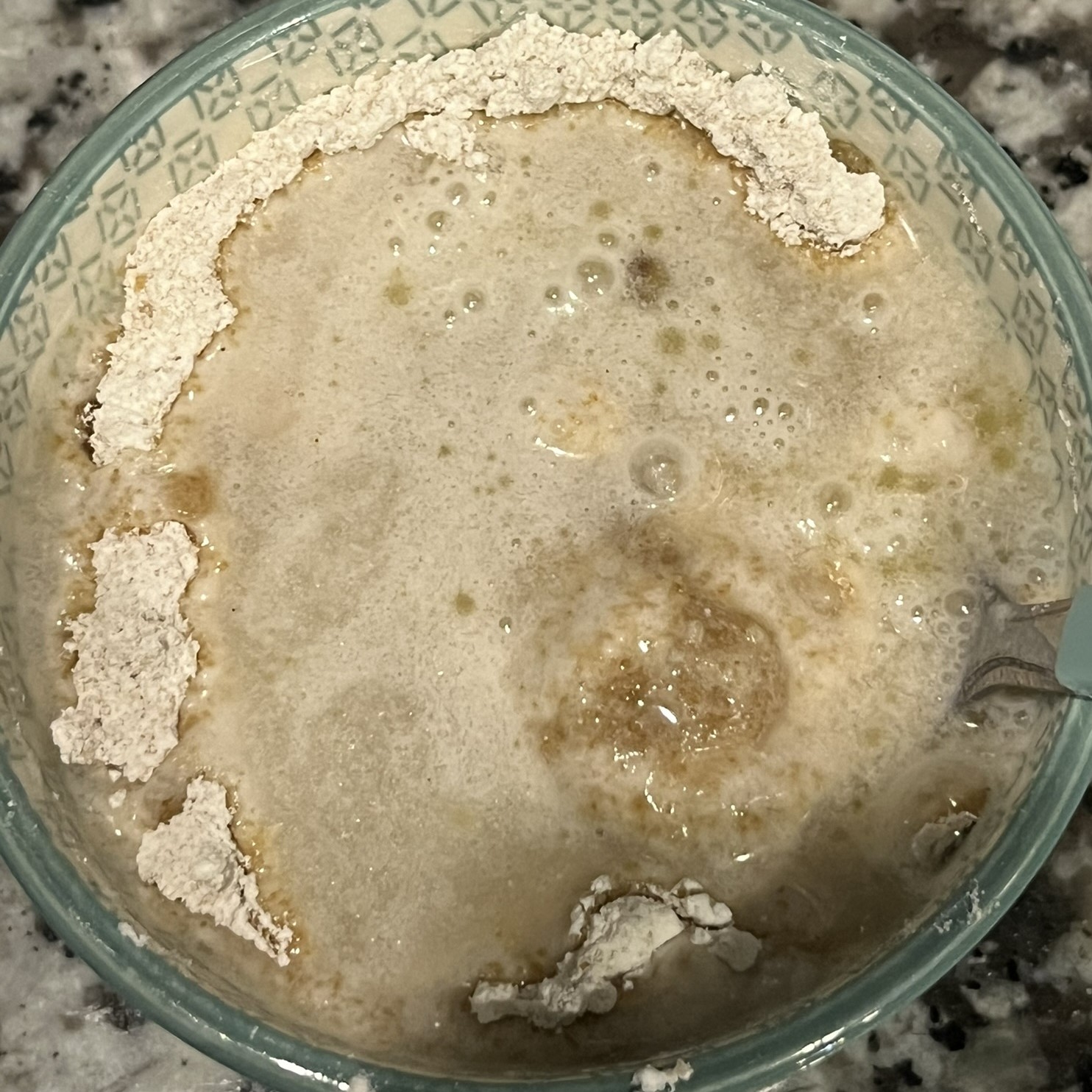 small, green and white ceramic bowl with water, vinegar, vanilla, and olive oil added to the dry ingredients
