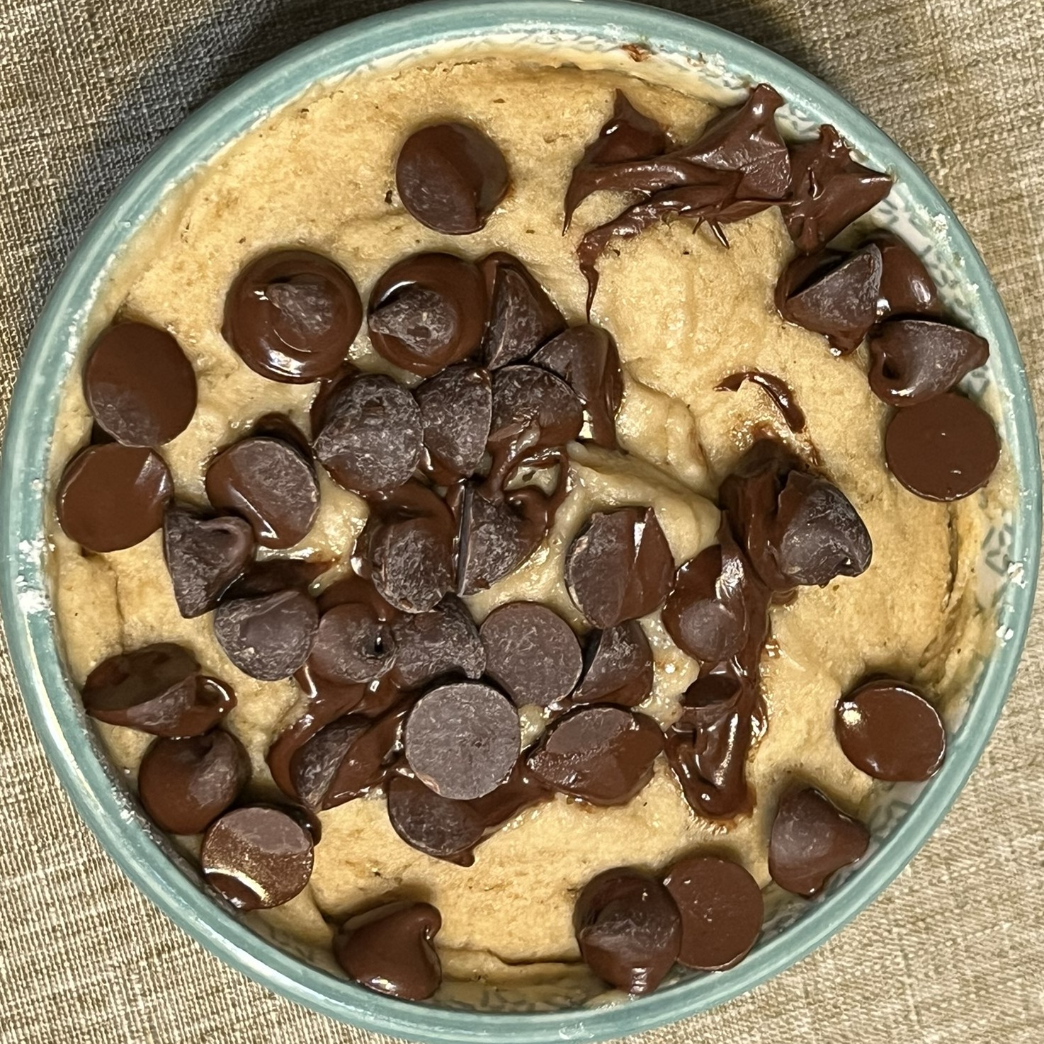 small, green and white ceramic bowl with chocolate chips melting atop the warm mug cake