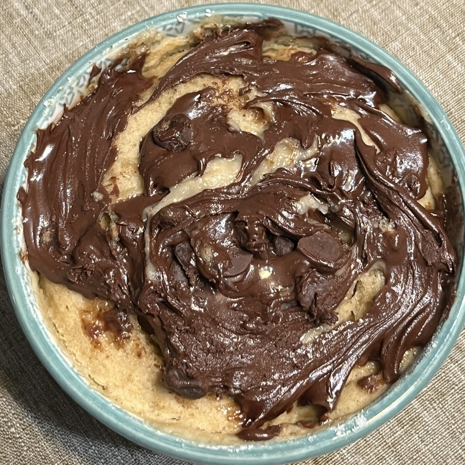 small, green and white ceramic bowl with melted chocolate spread on top of warm mug cake