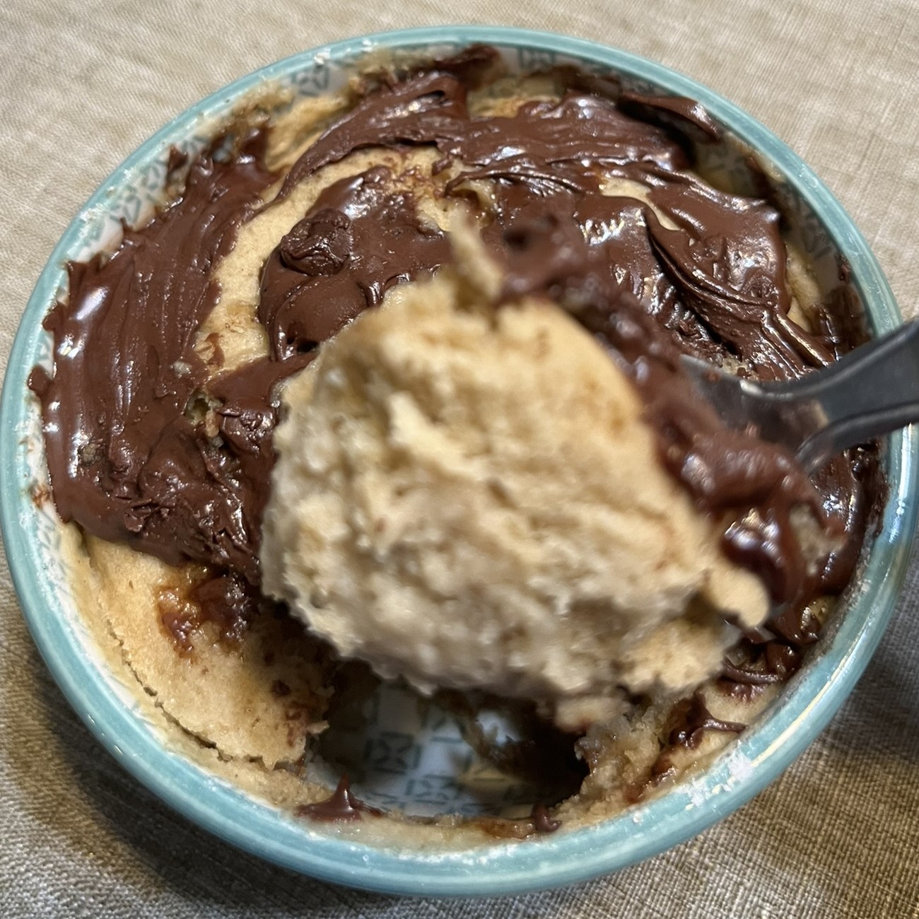 small, green and white ceramic bowl with vanilla, olive oil cake and melted chocolate. One spoonful is removed, ready for the first delicious bite.