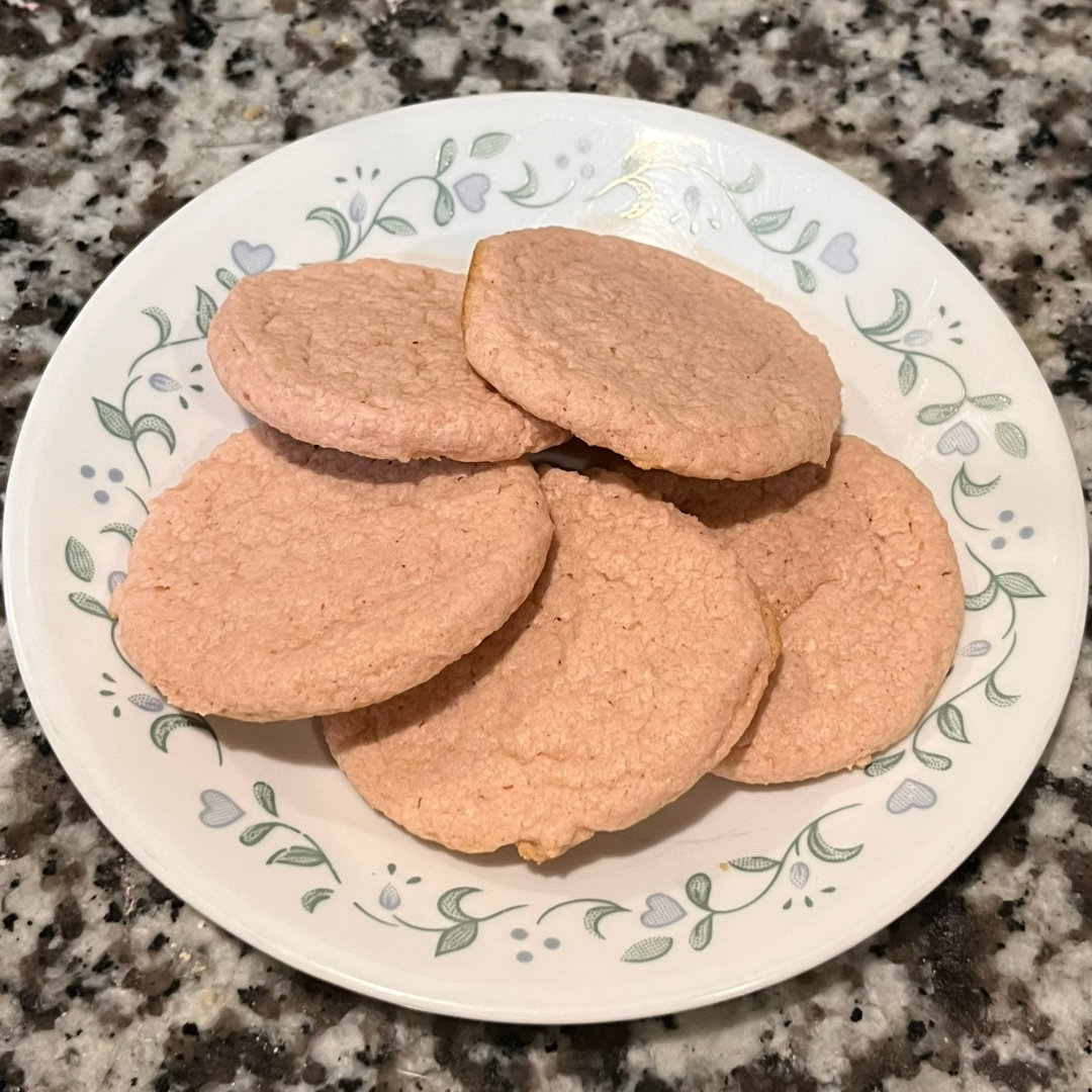 close-up photo of pink Watermelon Lime Sugar Cookies on a white plate with a blue and green flower border on a granite countertop