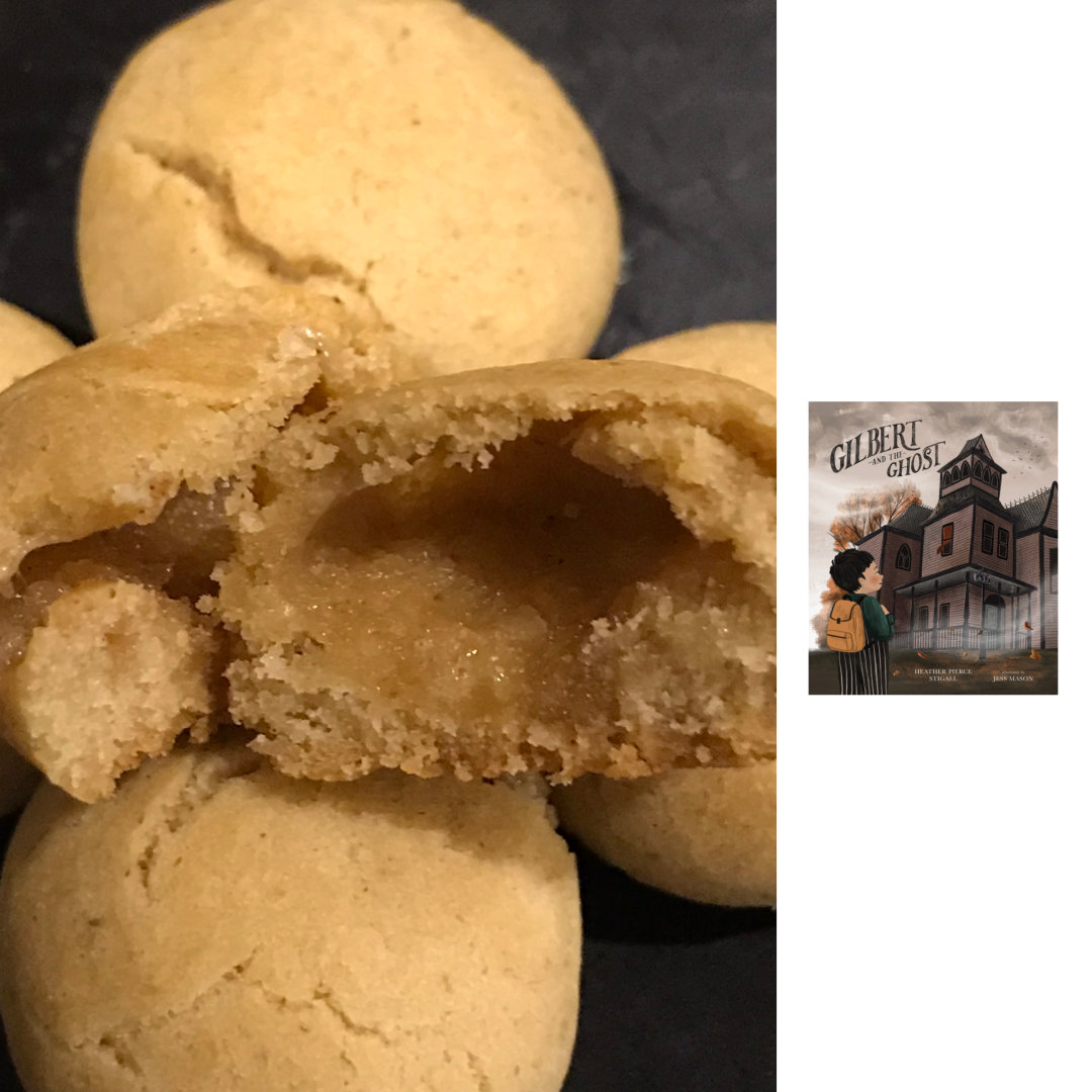 A cropped, close-up photo of Fall Phantoms Cookies, which are bite-sized maple cookies with a hollow center, on a black plate. To the right of the cookies, against a white background, is the illustrated book cover of GILBERT AND THE GHOST by Heather Pierce Stigall and Jess Mason. A boy with dark hair, wearing a green sweater, striped pants, and a yellow backpack, stares up at an old, slightly-spooky, house with the number 632 on it. The title is above the house, against a grey and cloudy sky.