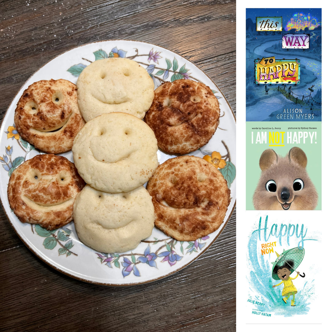 Photo of Happy Smiles Sugar Cookies - Three rows of sugar cookies with smiley faces cut into them on a white plate with a floral border. The middle row of smiles is unadorned. The rows on the right and left have been rolled in a mixture of cocoa powder and powdered sugar before baking, so they are darker. To the left of the photo is a vertical column of three book covers. At the top is THIS WAY TO HAPPY by Alison Green Myers. An illustrated image of a river, at nighttime, winding its way from the top right to the bottom left corner. Off in the distance, at the top right corner, is a brightly-lit amusement park with a Ferris wheel. The title is displayed on three billboards spaced along the river in hand-lettered fonts reminiscent of old-timey carnival or amusement park signage. There is a simple rope bridge across the river near the bottom of the cover, with the silhouette of one person standing on the bank and one crossing the bridge to the other side. In the middle is I AM NOT HAPPY by Caroline L. Perry and illustrated by Sydney Hanson. A close-up illustration of the face of a smiling quokka, with its adorable, big, bright eyes and puffy cheeks, against a teal background, with the title in bold, all-caps block text across the top. And at the bottom is HAPPY RIGHT NOW by Julie Berry and illustrated by Holly Hatam. A Black girl wearing a yellow dress and galoshes and holding a teal unicorn umbrella splashes in a giant puddle against a white background. The title, with the word Happy in large, teal, script letters sweeps across the top of the page from the splash wave of the puddle, and in smaller, yellow, all-caps block letters are the words Right Now just above the girl's umbrella.